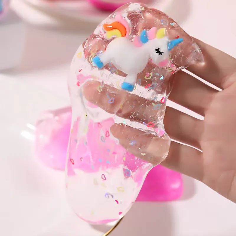 Prueba de estiramiento del Kit de Slime Transparente para Niños – una mano estira el slime transparente con un amuleto de unicornio y remolinos rosas para mostrar elasticidad.