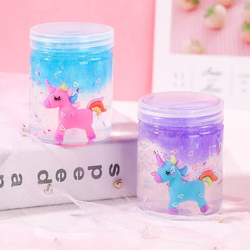 Kit de Slime Transparente para Niños – seis frascos pequeños de slime transparente pastel con amuletos de unicornio apilados sobre un libro para ver el conjunto completo.