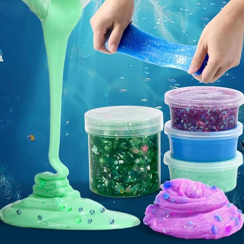 Demostración de textura del kit de slime de bricolaje con temática de galaxia con manos estirando slime azul, slime verde fluyendo y recipientes de slime con purpurina apilados.