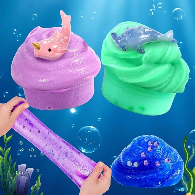 Kit de slime de bricolaje con temática de galaxia mostrado como una actividad práctica con slimes morado, verde y azul y juguetes de criaturas marinas bajo el agua.