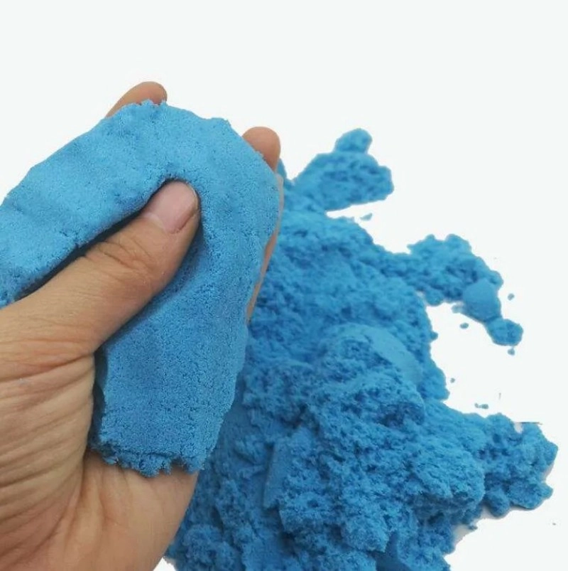 Primer plano de una mano apretando arena azul moldeable para mostrar textura suave y desmenuzable
