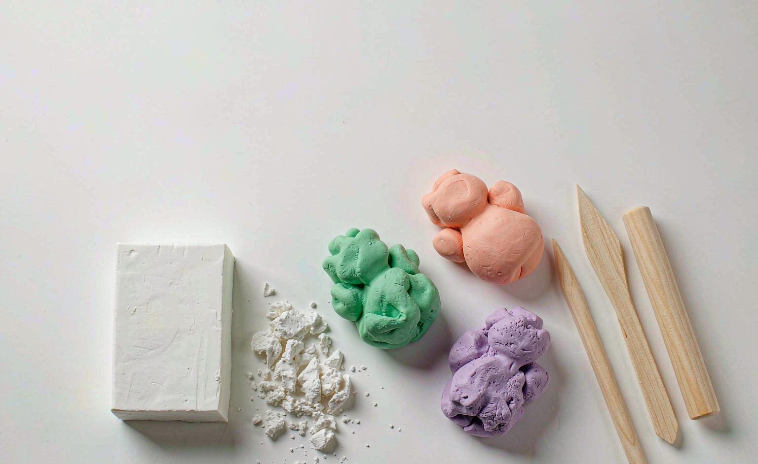 Air dry clay blocks, colored clay sculptures and wooden modeling tools on a white table