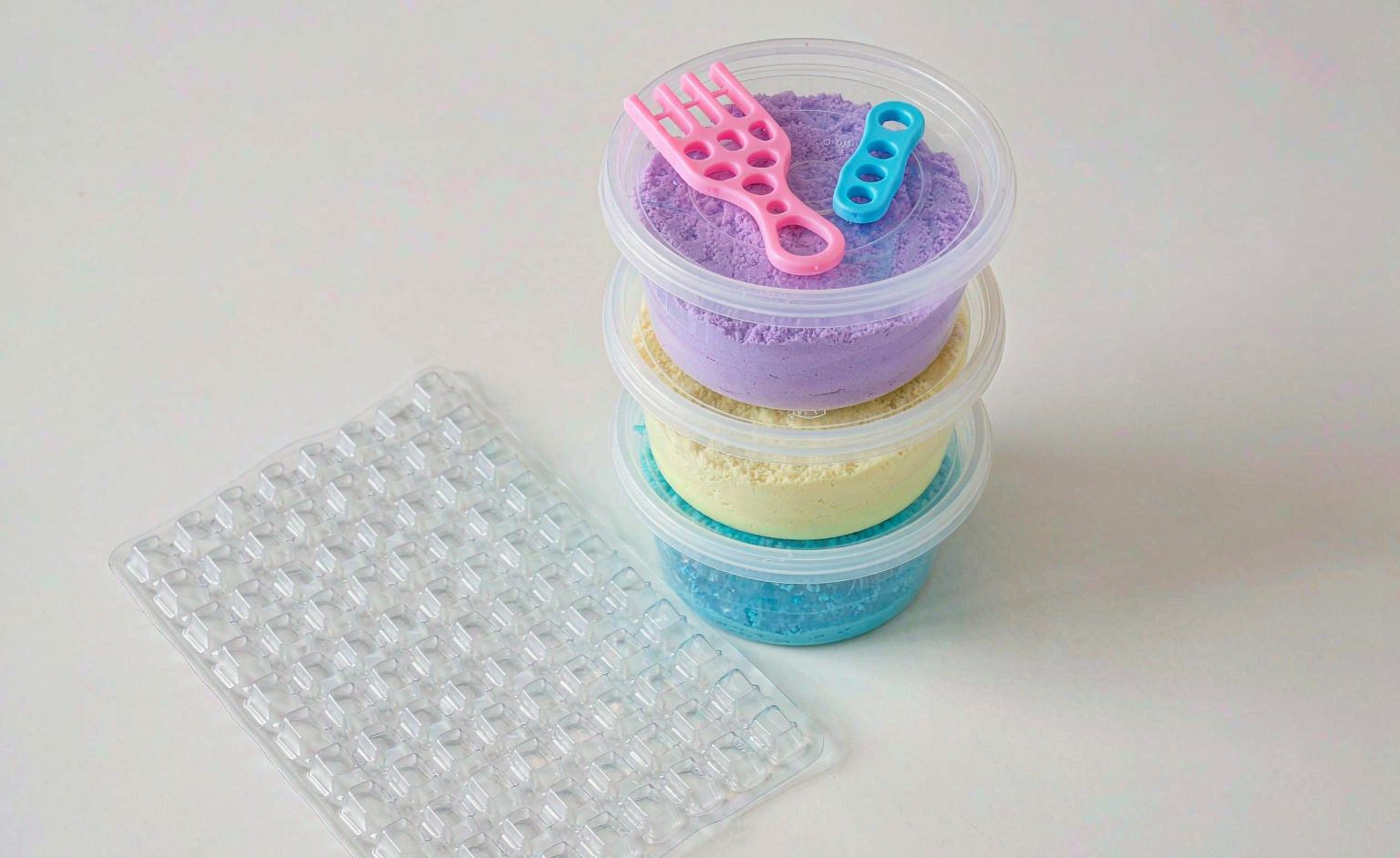 Stacked tubs of colorful kinetic sand with plastic molds and play tools