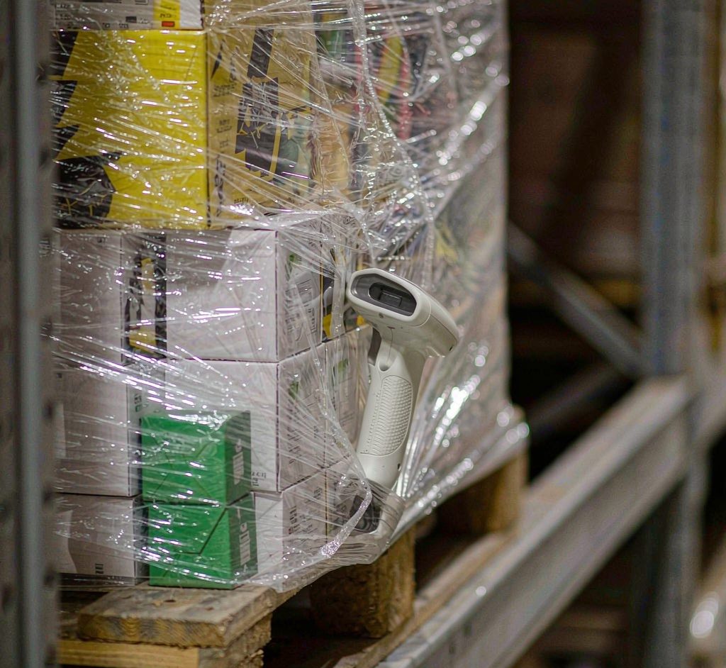 Barcode scanner checking a shrink-wrapped mixed pallet of toy cartons in a warehouse